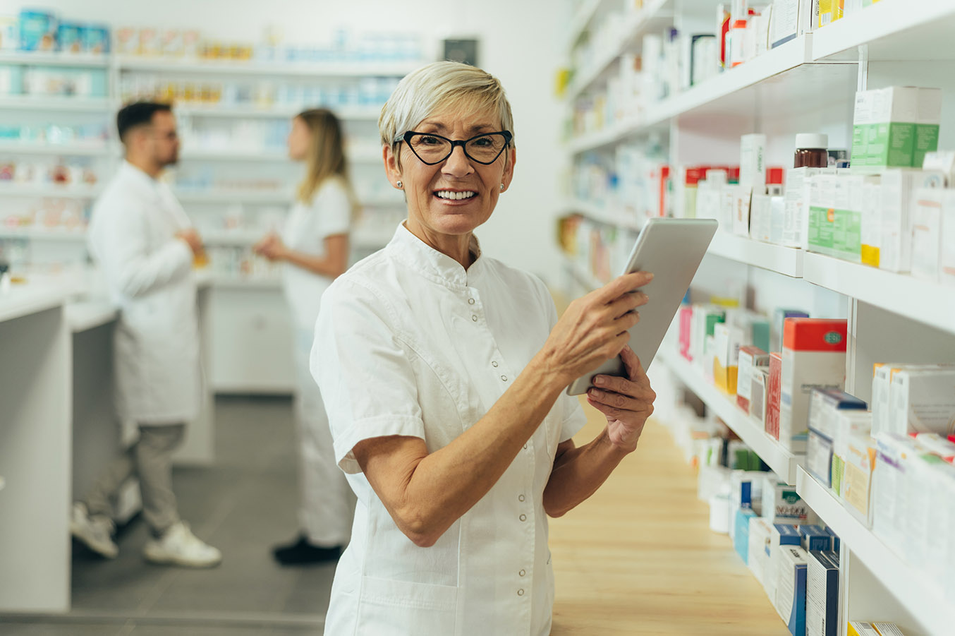 Smilende kvinne med briller og hvit frakk på apotek